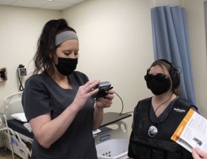 学生Logan Hadley（左）调整学生Mikayla Venable佩戴的听力模拟器的控制箱。